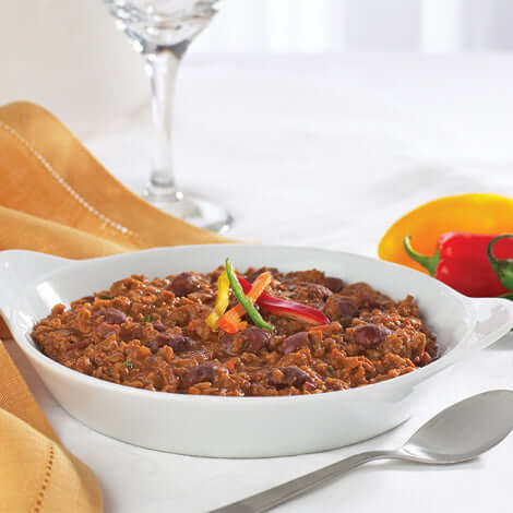 Hearty protein-rich entree served in a white dish, garnished with colorful peppers on a dining table.